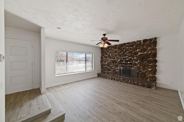 unfurnished living room with baseboards, a textured ceiling, a stone fireplace, and wood finished floors