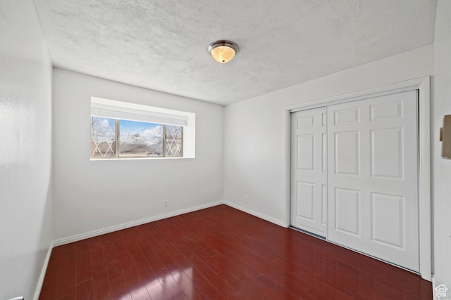 unfurnished bedroom featuring a closet, a textured ceiling, baseboards, and wood finished floors
