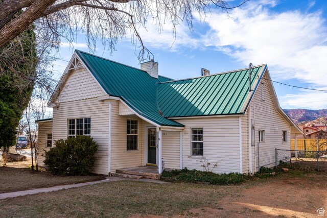 view of front facade with metal roof, a chimney, and fence