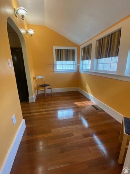 unfurnished room with baseboards, vaulted ceiling, wood finished floors, and arched walkways