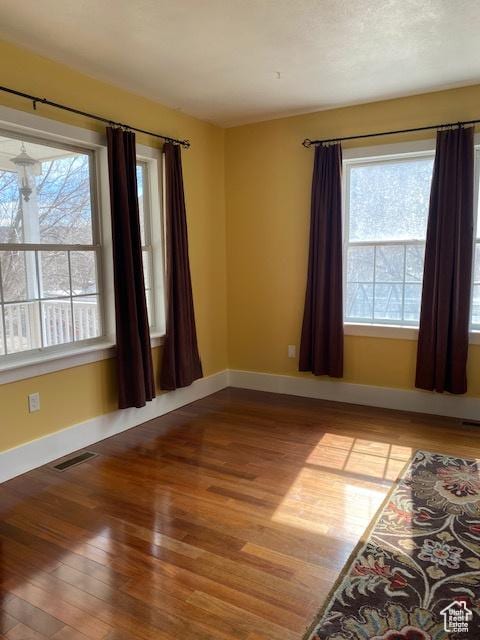 unfurnished room with baseboards, visible vents, and wood-type flooring