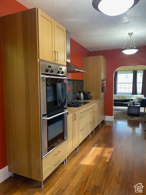 kitchen with black gas cooktop, tasteful backsplash, wood finished floors, stainless steel double oven, and arched walkways