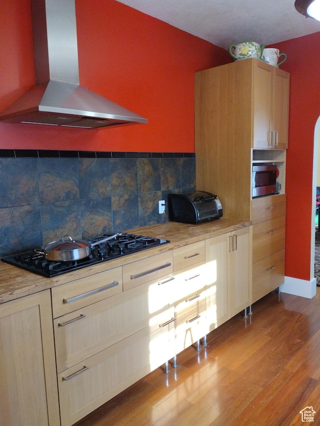 kitchen with light countertops, black gas cooktop, wall chimney exhaust hood, tasteful backsplash, and light wood-style floors