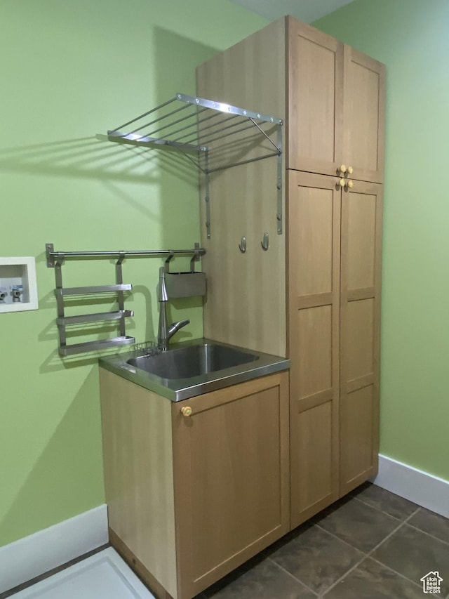 interior space featuring hookup for a washing machine, baseboards, dark tile patterned flooring, a sink, and cabinet space