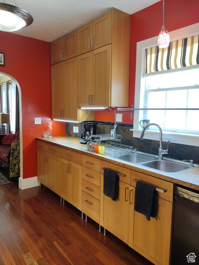 kitchen with dark wood finished floors, hanging light fixtures, a sink, arched walkways, and black dishwasher