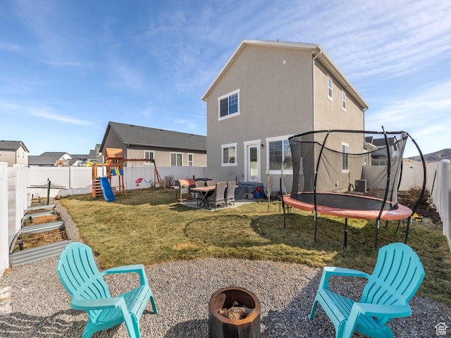 6119 N White Rock Rd, Eagle Mountain, UT 84005 - back of house featuring a trampoline, a fenced backyard, a playground, a yard, and a fire pit