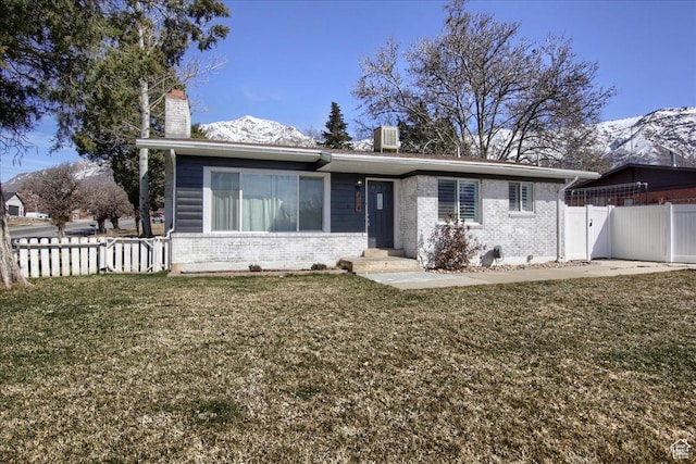 view of front of house featuring brick siding, a front lawn, fence, a chimney, and a mountain view