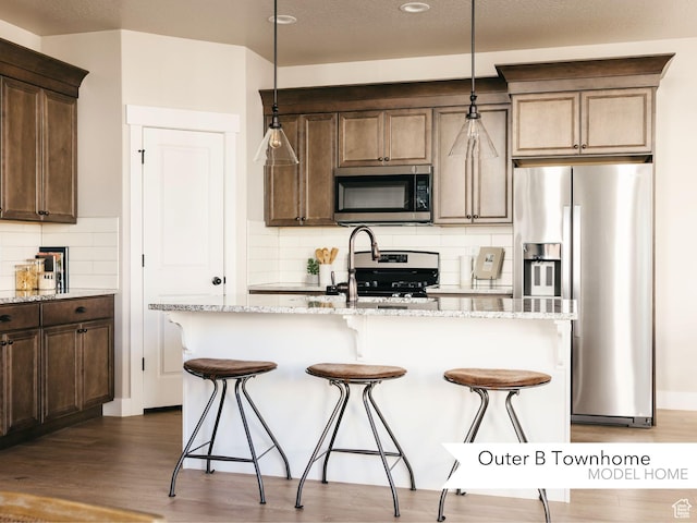 kitchen with tasteful backsplash, light stone countertops, appliances with stainless steel finishes, a kitchen bar, and dark wood-style floors