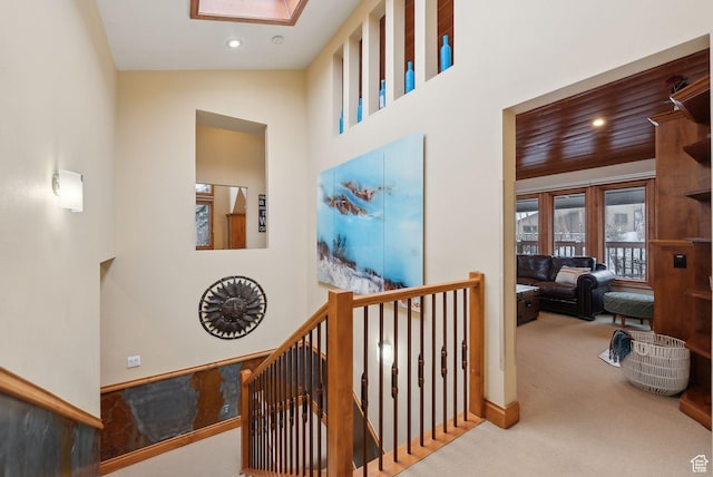 corridor featuring carpet, an upstairs landing, recessed lighting, a skylight, and a towering ceiling