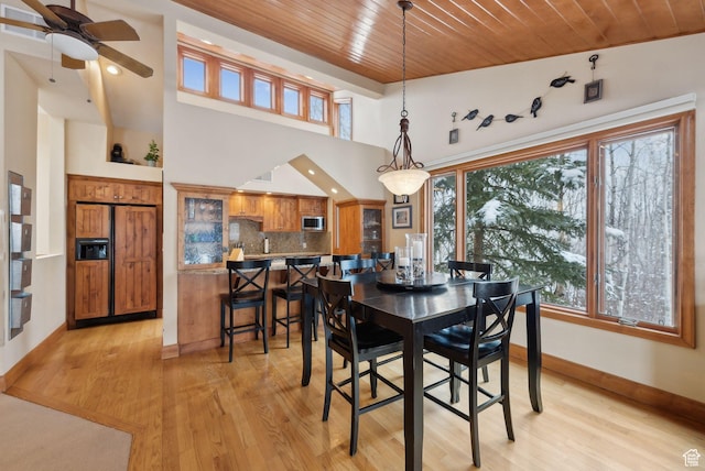 dining space with light wood-style flooring, baseboards, a high ceiling, and wooden ceiling