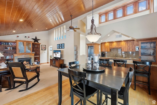 dining space featuring visible vents, light wood-style flooring, a lit fireplace, wooden ceiling, and baseboards