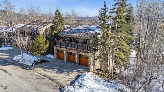 rustic home featuring stone siding, a balcony, driveway, and a garage