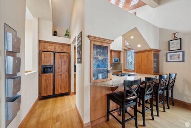 bar featuring light wood-style floors, tasteful backsplash, a towering ceiling, and baseboards