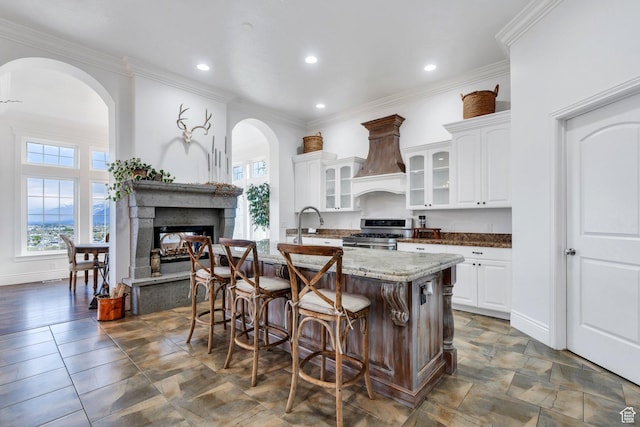 2382 S Spanish Oaks Dr, Spanish Fork, UT 84660 - kitchen with glass insert cabinets, stainless steel gas range oven, a kitchen bar, custom range hood, and a multi sided fireplace