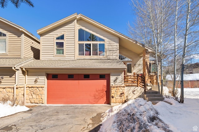 view of front of house featuring a garage, stone siding, driveway, and a shingled roof