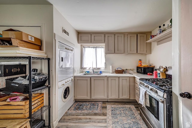 kitchen featuring a sink, black microwave, light countertops, stacked washer / dryer, and gas range
