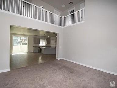 4929 W Red Ruby Ln, Herriman, UT 84096 - unfurnished living room featuring baseboards, dark carpet, and a towering ceiling