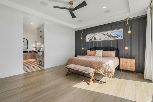 bedroom featuring a ceiling fan, a tray ceiling, wood finished floors, recessed lighting, and baseboards