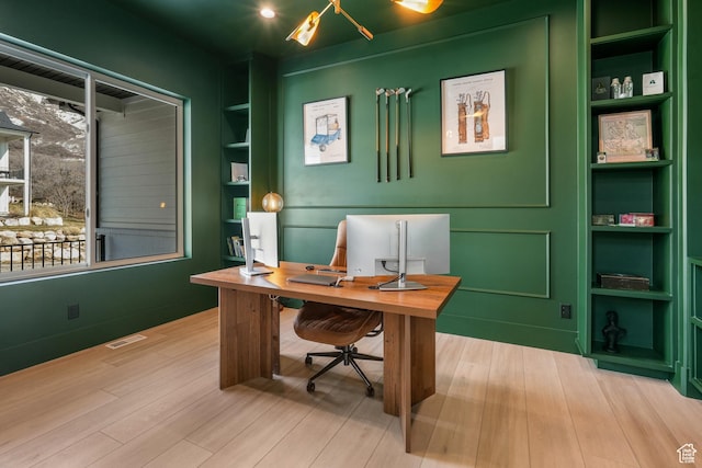 office space featuring visible vents, built in shelves, and wood finished floors