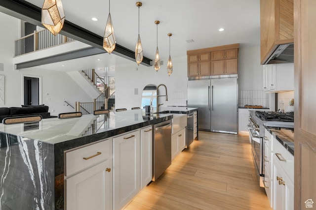 kitchen featuring dark stone countertops, high end appliances, light wood finished floors, decorative backsplash, and a large island