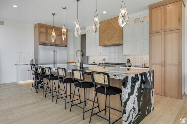 kitchen with custom exhaust hood, tasteful backsplash, light wood finished floors, and stainless steel built in refrigerator