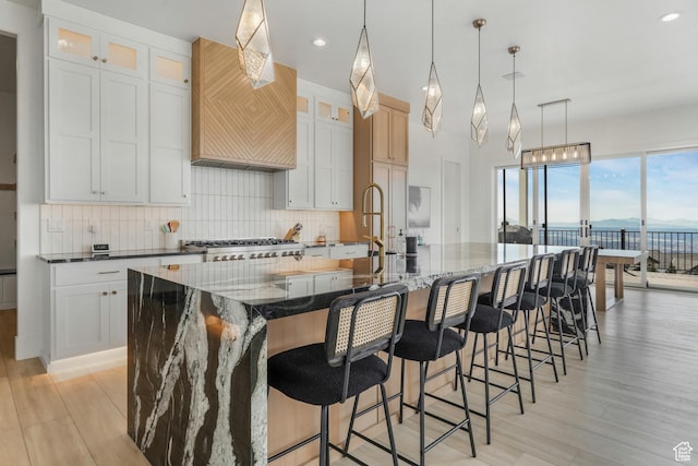 kitchen featuring a spacious island, glass insert cabinets, dark stone counters, light wood-type flooring, and decorative backsplash