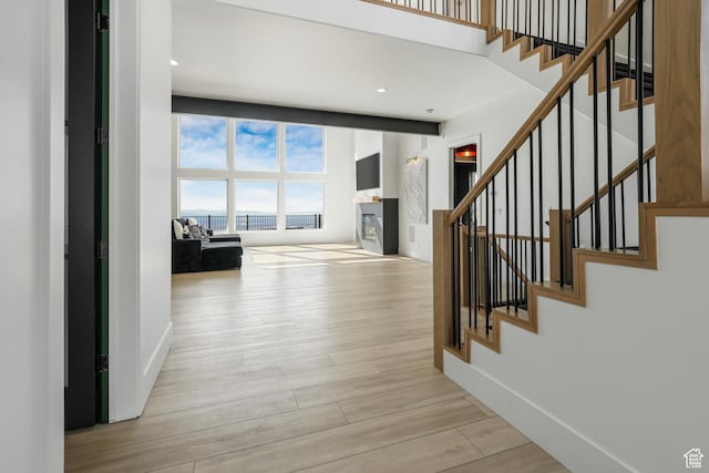 hallway featuring a towering ceiling, stairs, baseboards, and wood finished floors