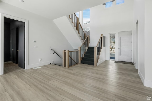 entrance foyer featuring baseboards, light wood-style floors, and a towering ceiling