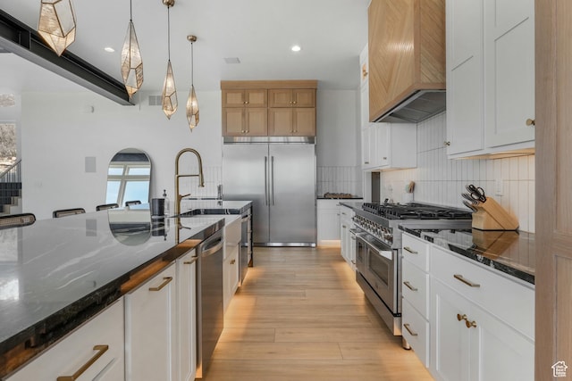 kitchen with light wood-type flooring, custom exhaust hood, dark stone counters, high quality appliances, and tasteful backsplash