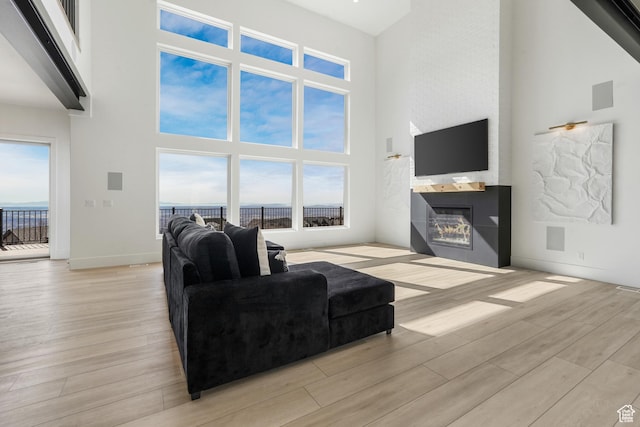 living area with visible vents, a large fireplace, baseboards, a high ceiling, and light wood-style floors