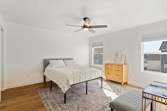 bedroom featuring a ceiling fan, wood finished floors, baseboards, and a textured ceiling