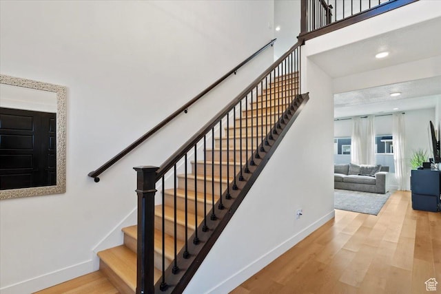 stairway with a high ceiling, recessed lighting, wood finished floors, and baseboards