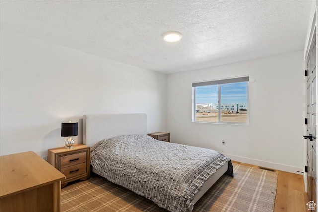 bedroom with visible vents, wood finished floors, baseboards, and a textured ceiling