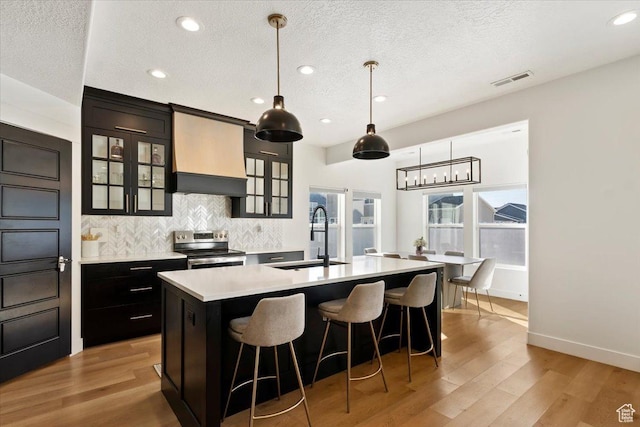 kitchen with a center island with sink, electric stove, a sink, backsplash, and light countertops