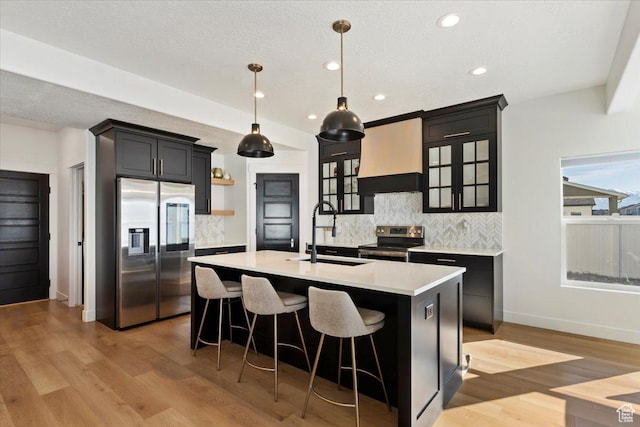 kitchen with a sink, premium range hood, light countertops, appliances with stainless steel finishes, and open shelves