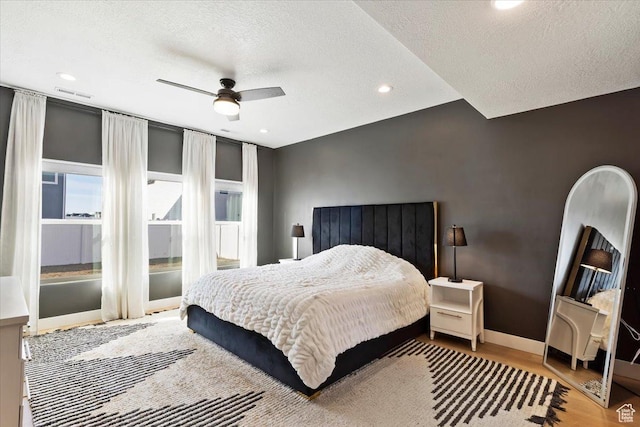 bedroom with visible vents, a textured ceiling, wood finished floors, baseboards, and ceiling fan
