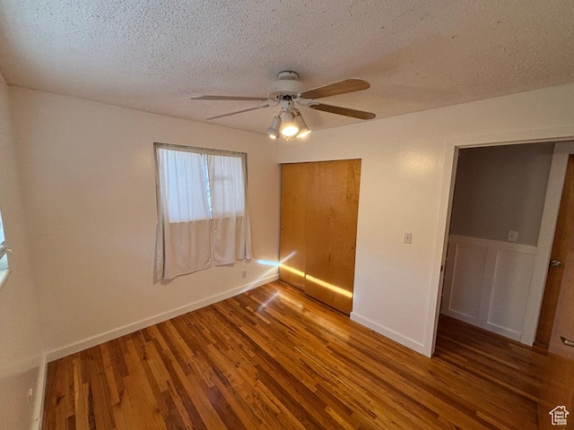 unfurnished bedroom with a ceiling fan, baseboards, wood finished floors, a closet, and a textured ceiling
