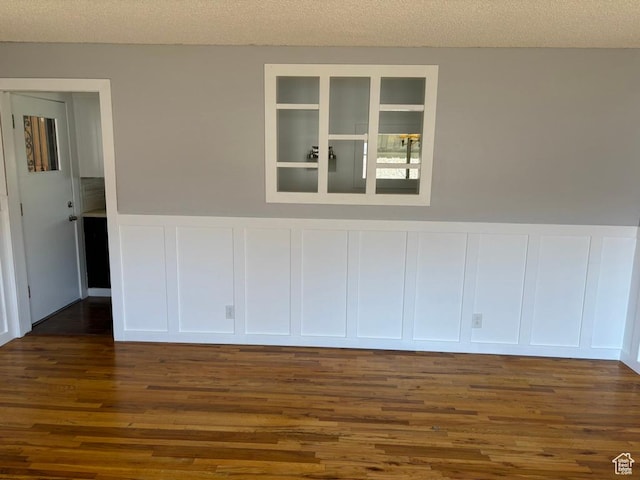 unfurnished room featuring a decorative wall, wainscoting, a textured ceiling, and dark wood-style flooring