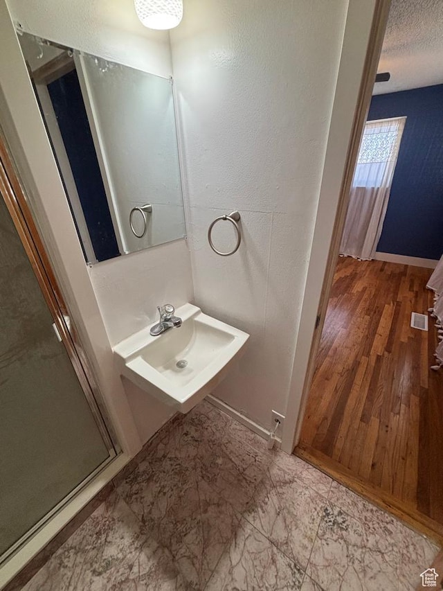 bathroom featuring baseboards, visible vents, a sink, a shower stall, and a textured ceiling