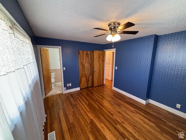 unfurnished bedroom with wood finished floors, baseboards, visible vents, a textured ceiling, and connected bathroom