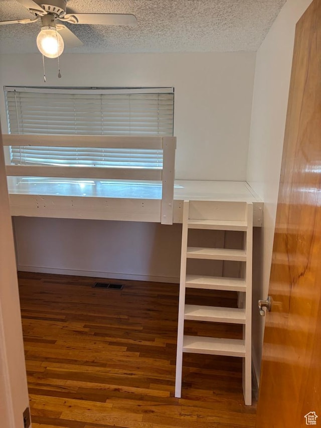 interior space featuring a ceiling fan, wood finished floors, visible vents, and a textured ceiling