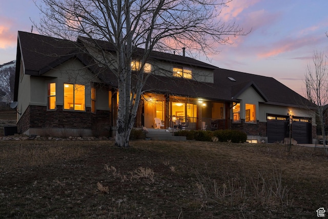 back of property featuring a porch, a garage, central AC unit, and stone siding
