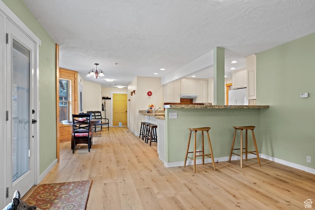 1762 S Hobblecreek Haven Rd, Springville, UT 84663 - kitchen featuring freestanding refrigerator, under cabinet range hood, a textured ceiling, light wood-style floors, and a kitchen breakfast bar