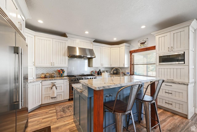13862 S 7300 W, Herriman, UT 84096 - kitchen featuring built in appliances, wall chimney exhaust hood, a breakfast bar area, decorative backsplash, and a textured ceiling