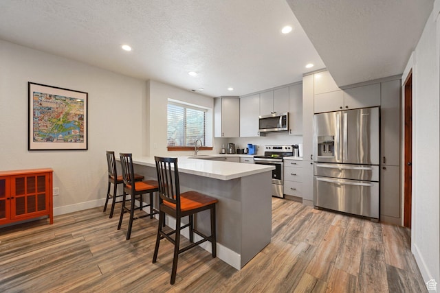 13862 S 7300 W, Herriman, UT 84096 - kitchen featuring stainless steel appliances, light wood-style flooring, a kitchen breakfast bar, a peninsula, and recessed lighting