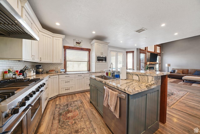 13862 S 7300 W, Herriman, UT 84096 - kitchen featuring appliances with stainless steel finishes, exhaust hood, open floor plan, light wood-type flooring, and recessed lighting