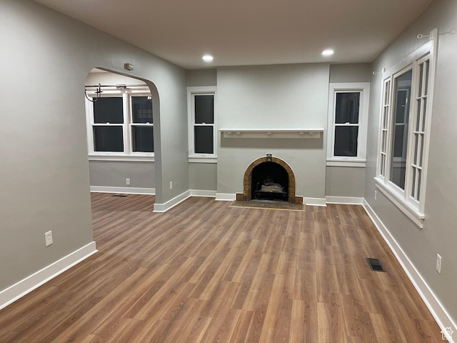 unfurnished living room featuring visible vents, a brick fireplace, baseboards, wood finished floors, and arched walkways