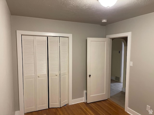 unfurnished bedroom with visible vents, baseboards, wood finished floors, a closet, and a textured ceiling