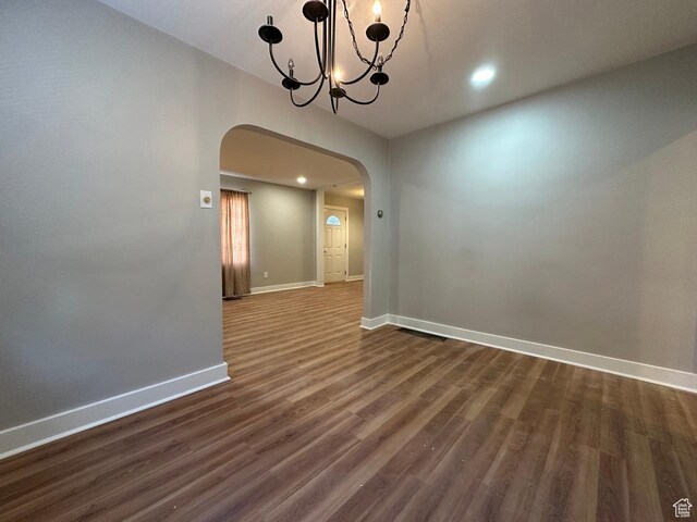 spare room with dark wood-style floors, recessed lighting, arched walkways, baseboards, and a chandelier