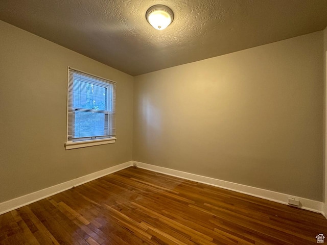 empty room featuring a textured ceiling, baseboards, and dark wood-style flooring